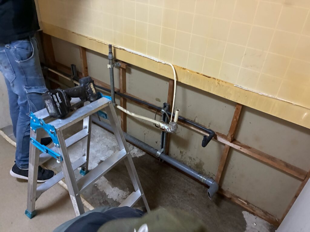 既存のキッチン本体の解体および屋外への搬出撤去が完了し普段は隠れている壁面や床下の各種配管が露出した状態の様子です。壁面に残っている給水管や給湯管そして排水管などは新しく設置するクリナップのシステムキッチンであるラクエラの図面仕様に合わせてこの後適切な位置へと切り回しをおこなう重要な工程へと移ります。
