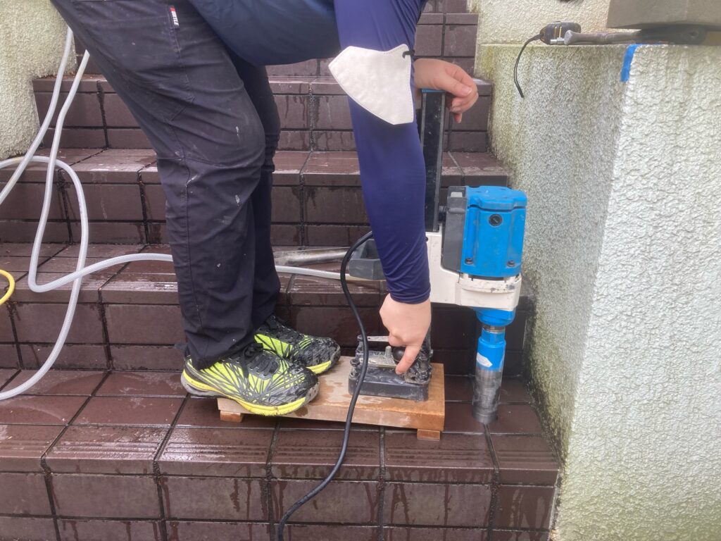 手すりの支柱を立てるため、専用のコア抜き機を用いて階段のタイルに円筒状の穴をあけている様子です。土台に柱をしっかりと埋め込んで固定し、体重をかけても決してグラつかない強固な手すりを作り上げます。