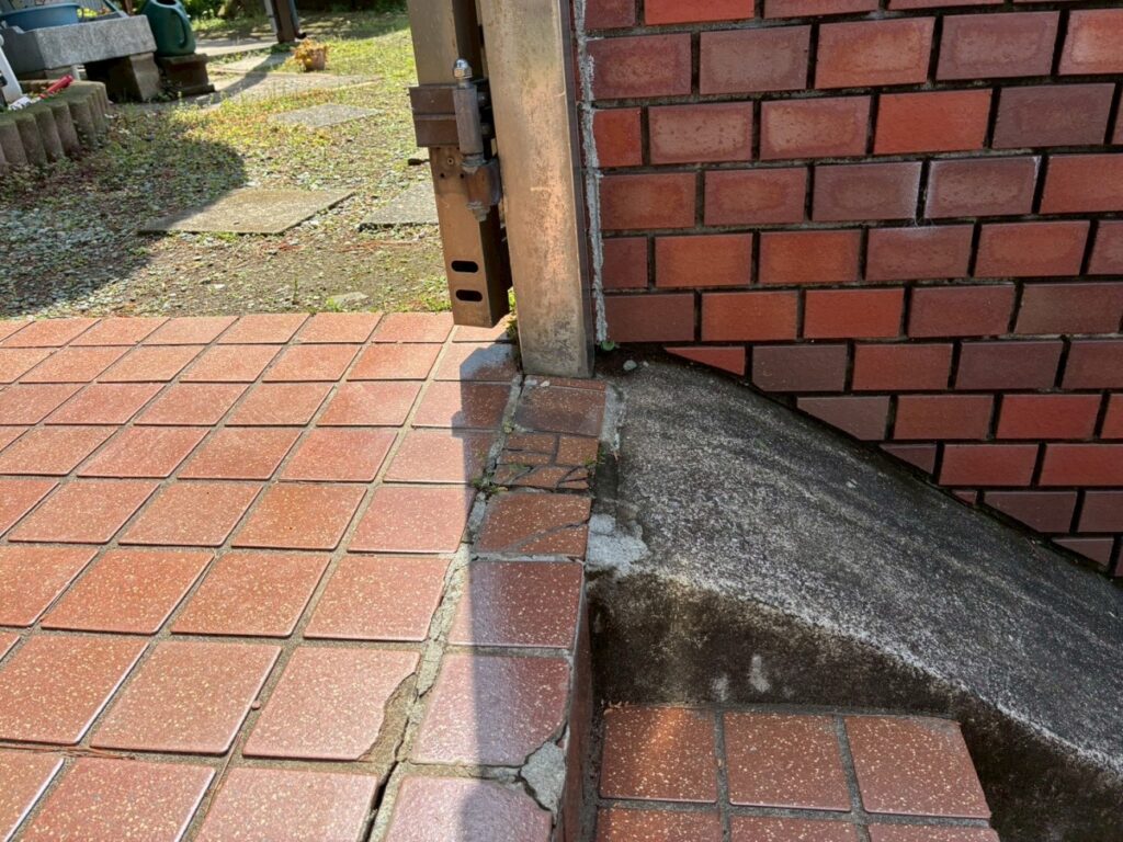 施工前のアプローチ階段部分のタイル写真です。門扉の足元や階段の段鼻（角の部分）など、複数箇所で経年劣化によるタイルの割れや外れ、浮きが発生しているのが見受けられました。このようなタイルの欠損は、見た目の美しさを損なうだけでなく、つまずきや転倒の原因となり大変危険です。今回は門扉の交換に合わせて、階段最上段の手前や2段目などの傷んでいるタイルを撤去し、安全のためにしっかりと下地から張り替え工事を実施します。