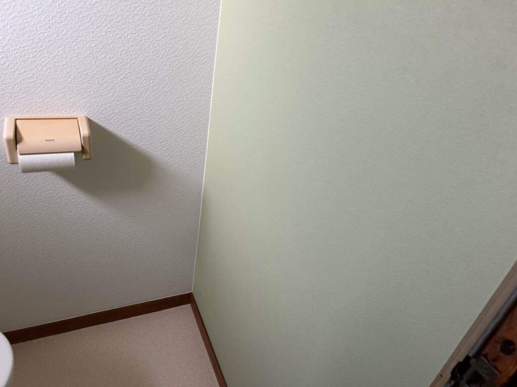 施工後のトイレ壁面です。設備交換に伴い、壁と天井のクロス張り替えを実施しました。淡いグリーンのアクセントクロスを採用し、清潔感と落ち着きのある空間へと整えています。